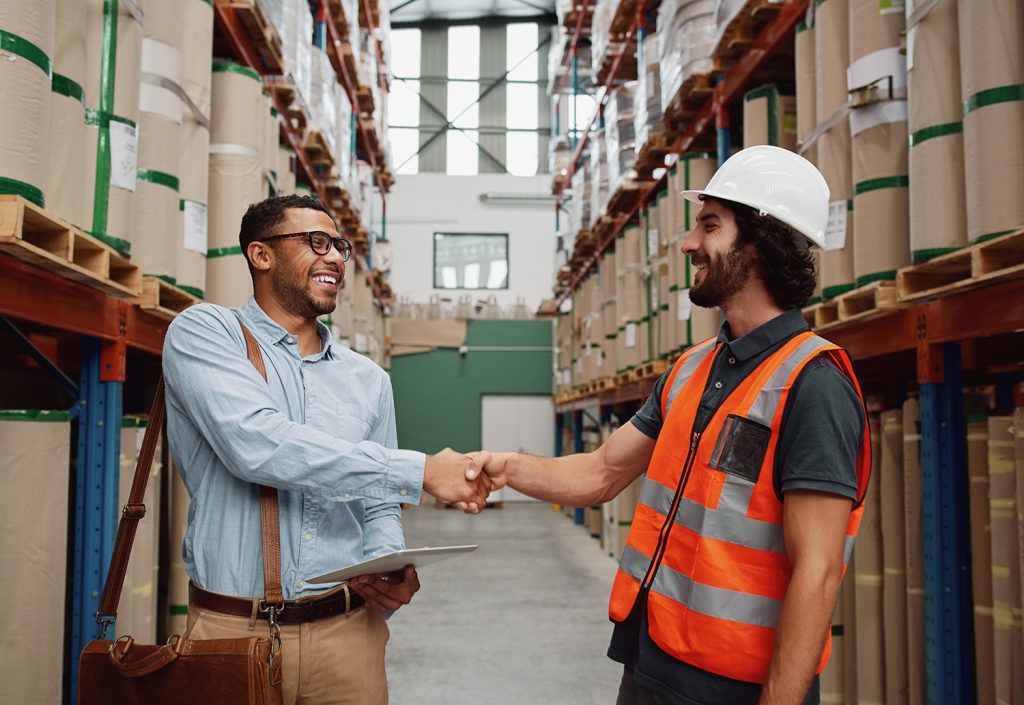 Happy business partner greeting warehouse worker in large-scale factory - banker grants factory worker his loan